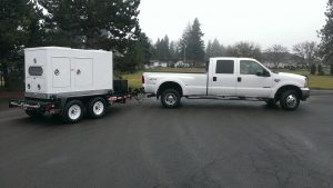 A white MQ EGS500C Studio Generator being towed by a white pickup truck.