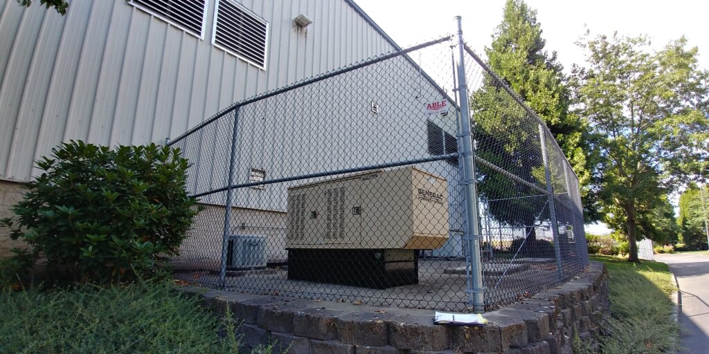 A generac diesel standby generator behind a fence and next to a building