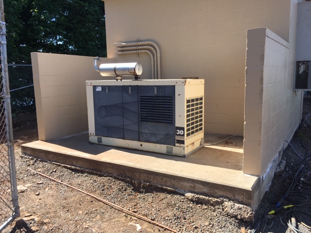 An industrial Kohler standby generator with an exhaust in a brick enclosement