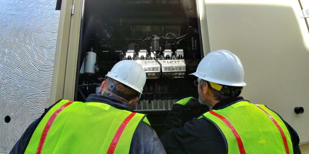 Two technicians looking into an industrial standby generator