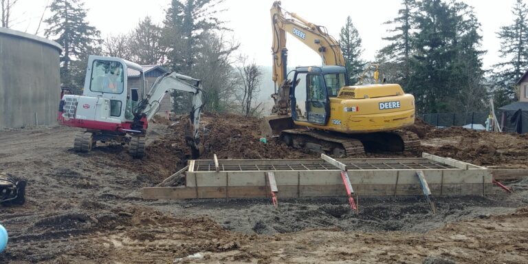 A concrete pad being poured for a standby generator installation with two excavators in the dirt