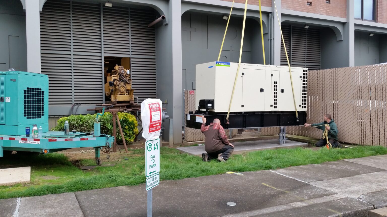 Two generator technicians helping lower an industrial AKSA standby generator